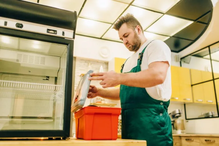 SMS Appliances worker with toolbox repair refrigerator at home in Okotoks.